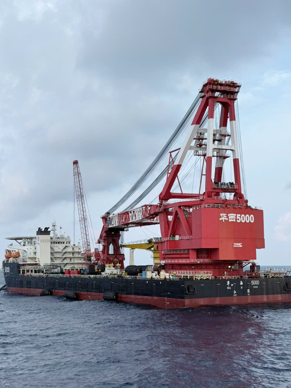 Red heavy-lift crane vessel Hua Xi 5000 with ZPMC branding at sea under an overcast sky