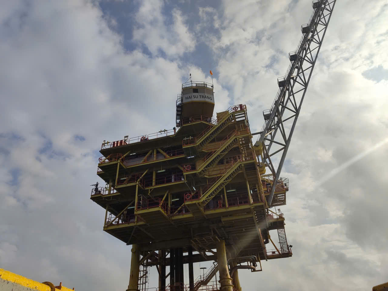 Yellow offshore platform structure labeled Hai Su Trang against a bright sky, with crane boom visible
